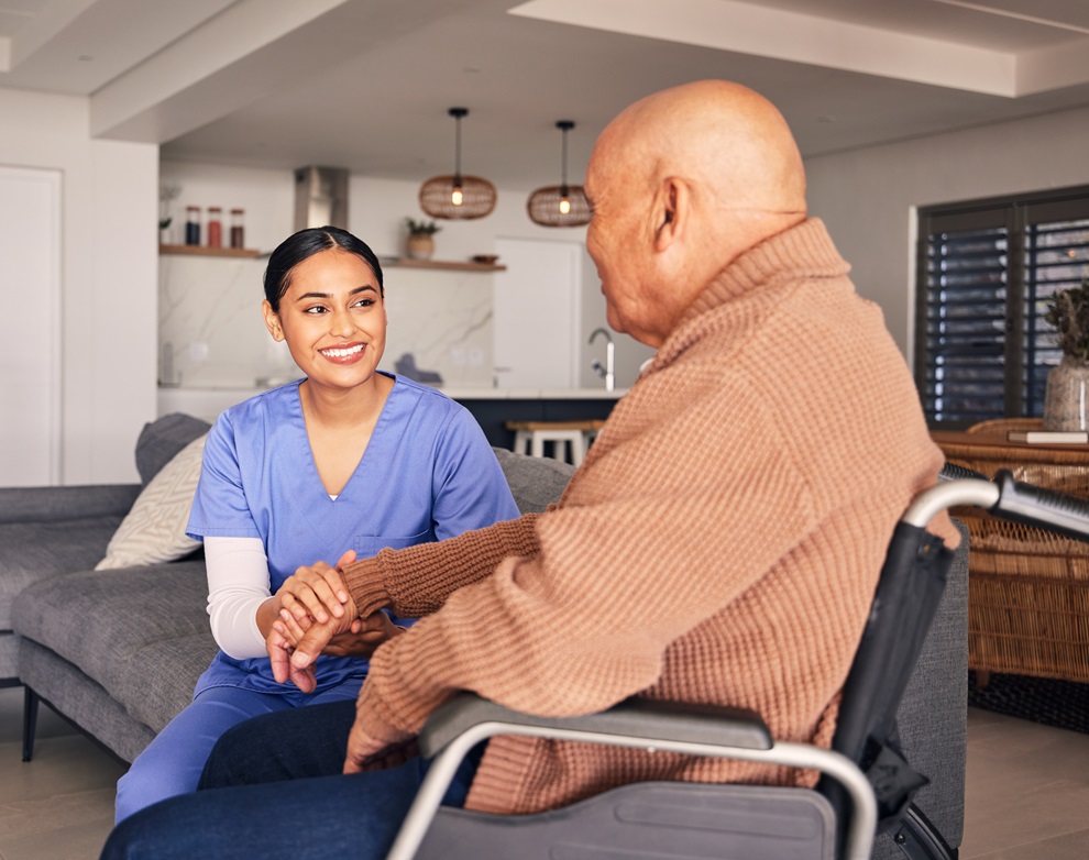 A carer holding hands with a man in his wheelchair at home