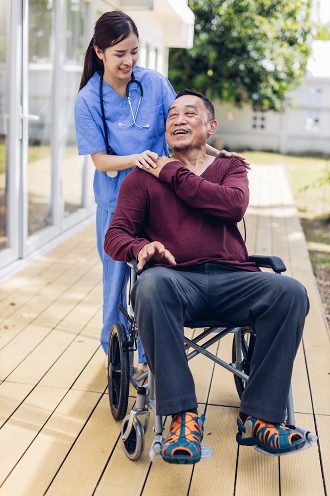 A companion walking outdoors with a man in his wheelchair